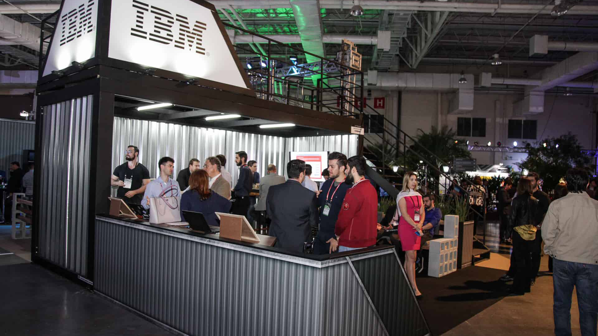 Container feito para a IBM, galvanizado e colunas pretas. Pessoas conversam dentro dele.